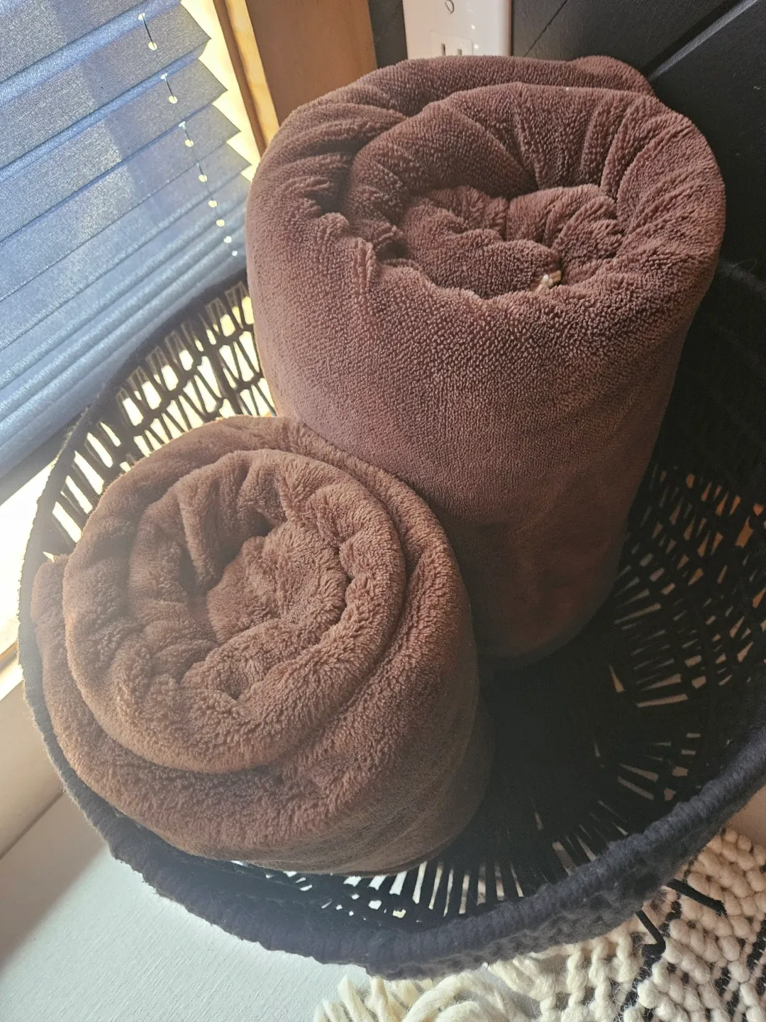 Two brown towels neatly arranged in a basket on a rug, representing a cleaning services setting.
